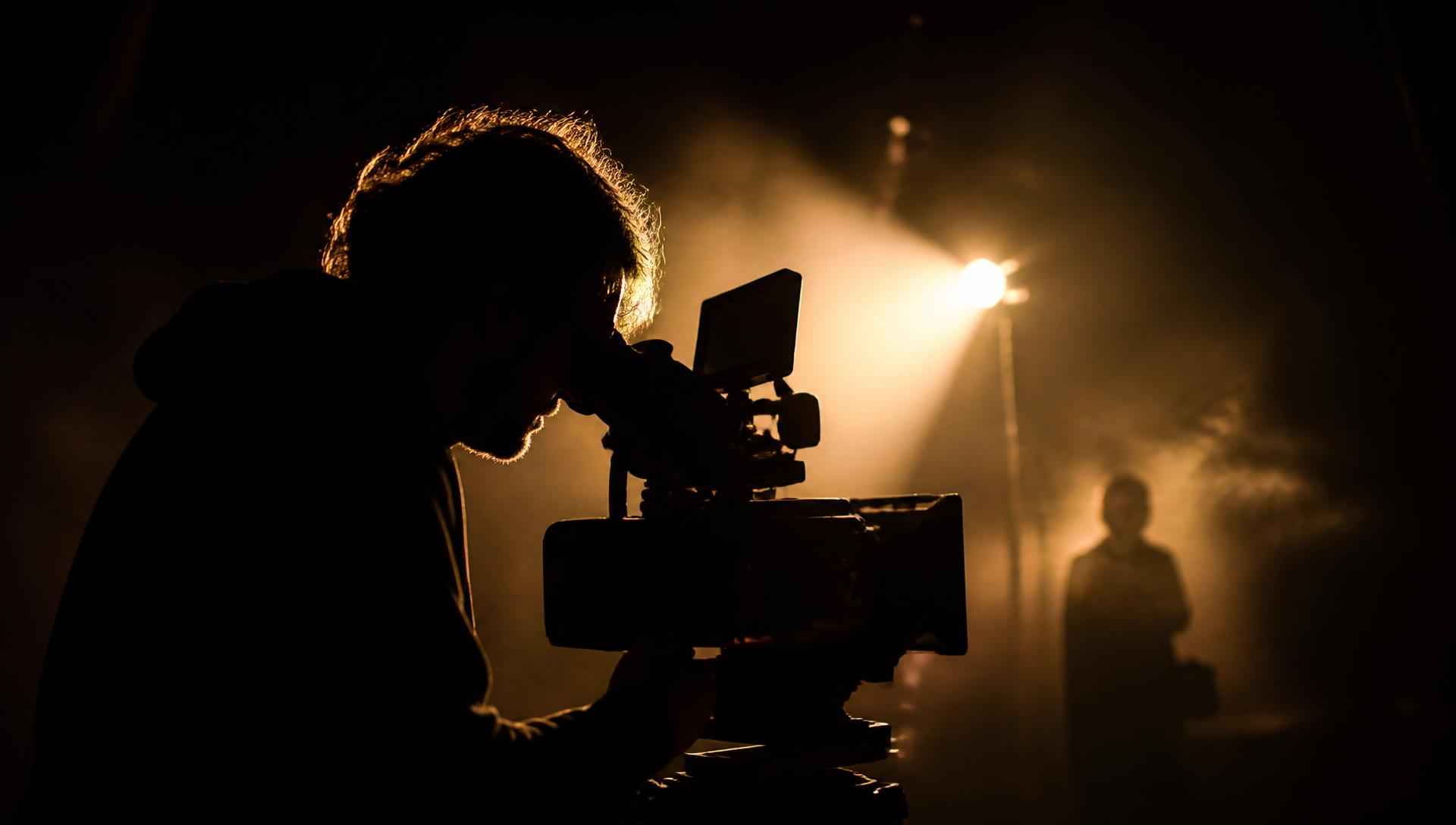 Cinematographer silhouetted behind a cinema camera on a dark film set
